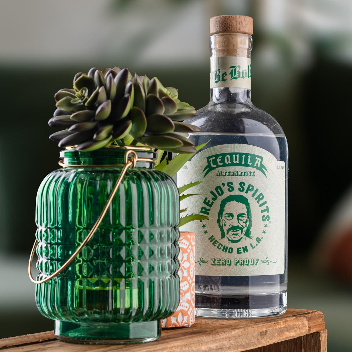 Tequila Alternative bottle next to a green glass lantern with a succulent
